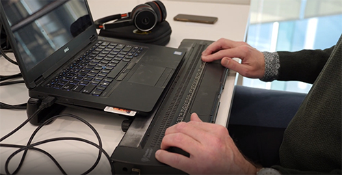 Medewerker aan het werk met laptop en daarvoor een brailletoetsenbord