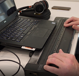 Medewerker aan het werk met laptop en daarvoor ligt een braille toetsenbord