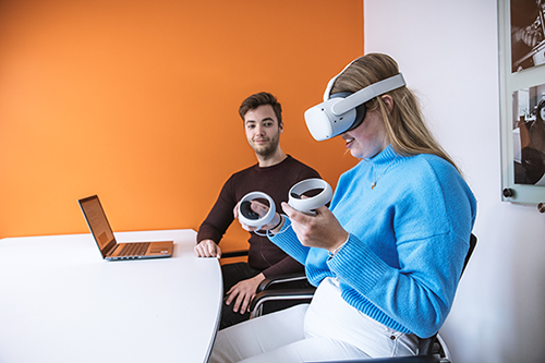 Kandidaat heeft VR bril op en twee consoles in haar hand