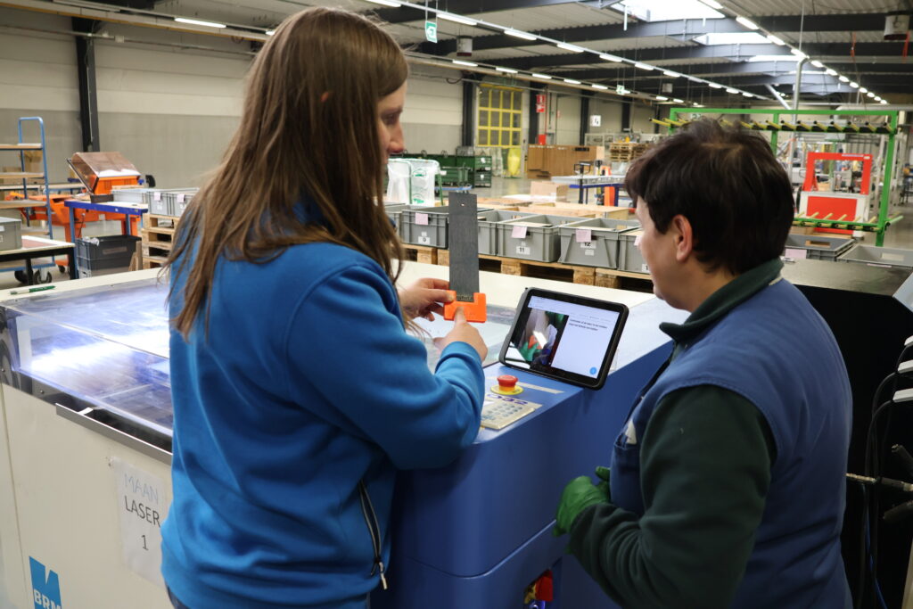 Een medewerker krijgt uitleg van An Defossez over het gebruik van de digitale werkinstructies.